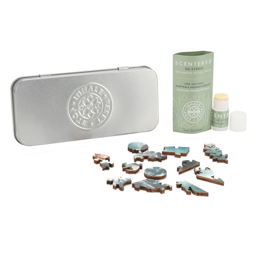 Parts of puzzle laid in front of silver tin and Scentered De-stress Mini balm with cap off next to balm sleeve.