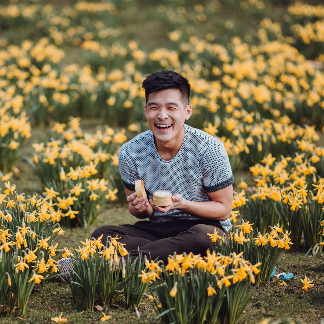 Scentered Happy Travel candle being held by a man in a field of yellow flowers.