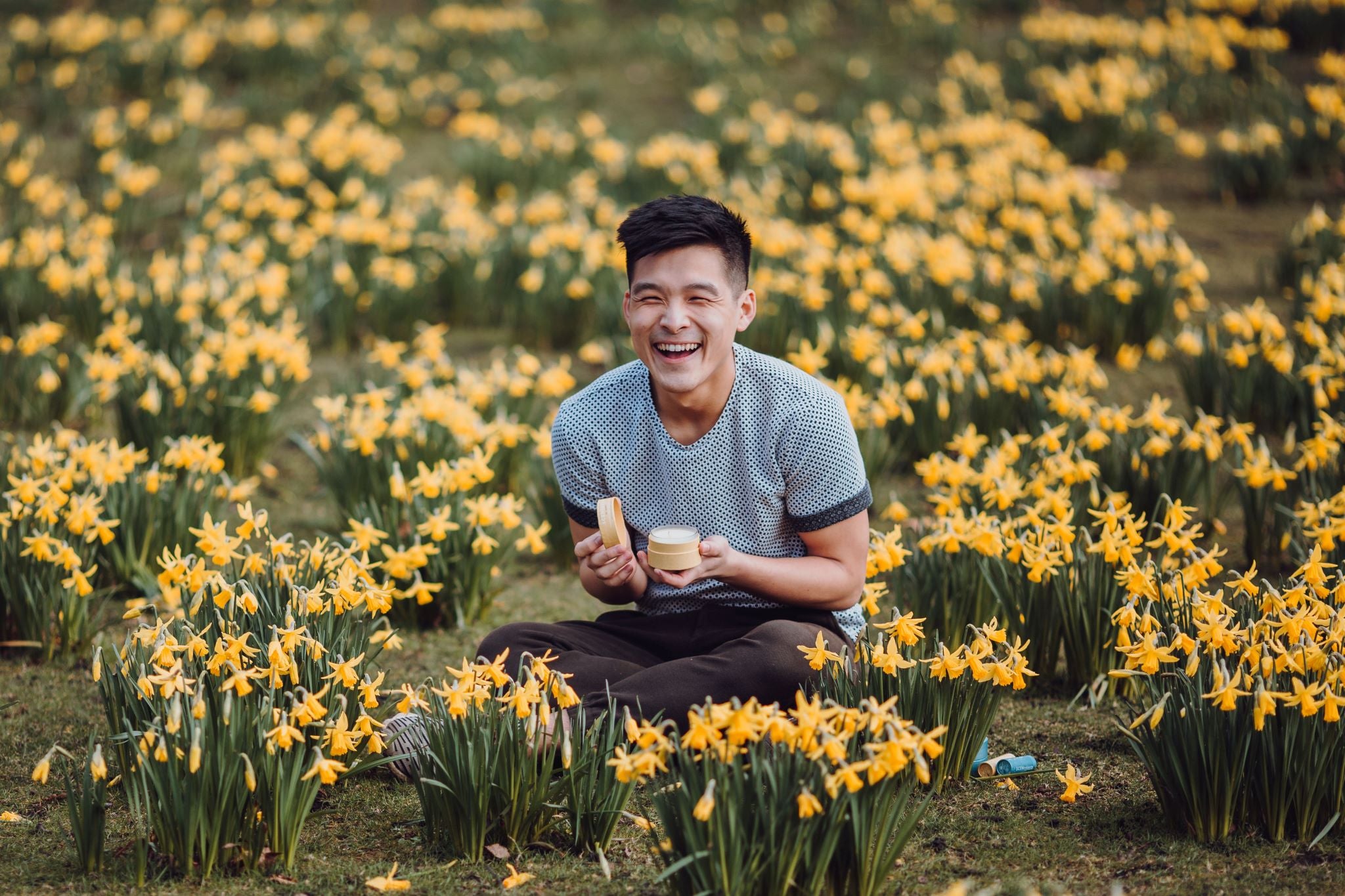 Scentered Happy Travel candle being held by a man in a field of yellow flowers.