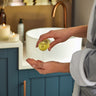  Lady wearing a bathrobe, pouring Scentered Sleep Well Oil for Body, Bath & Shower into her hand while standing next to a sink